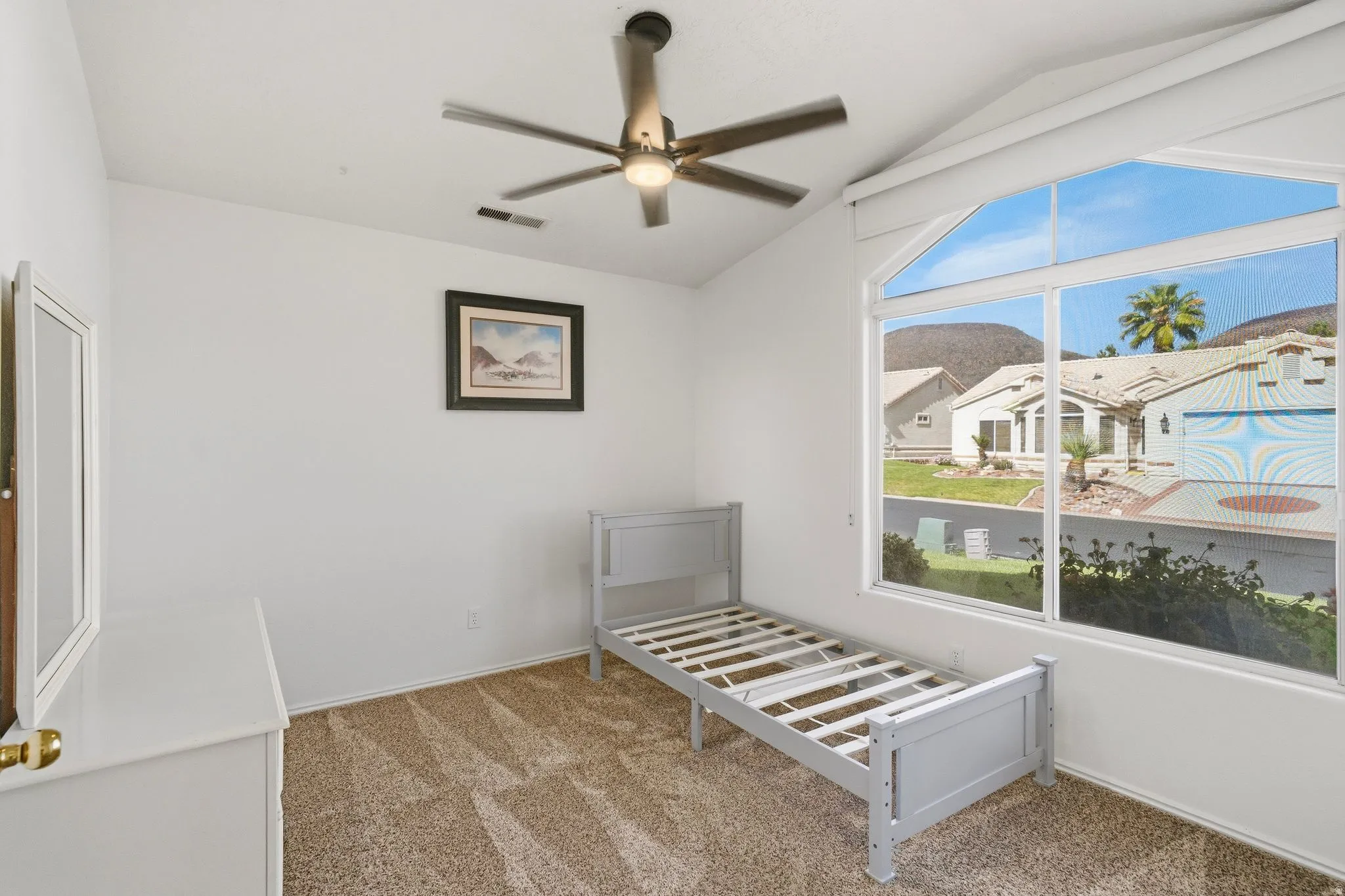 Vaulted ceiling room featuring a large arched window, ceiling fan, and patterned carpeting