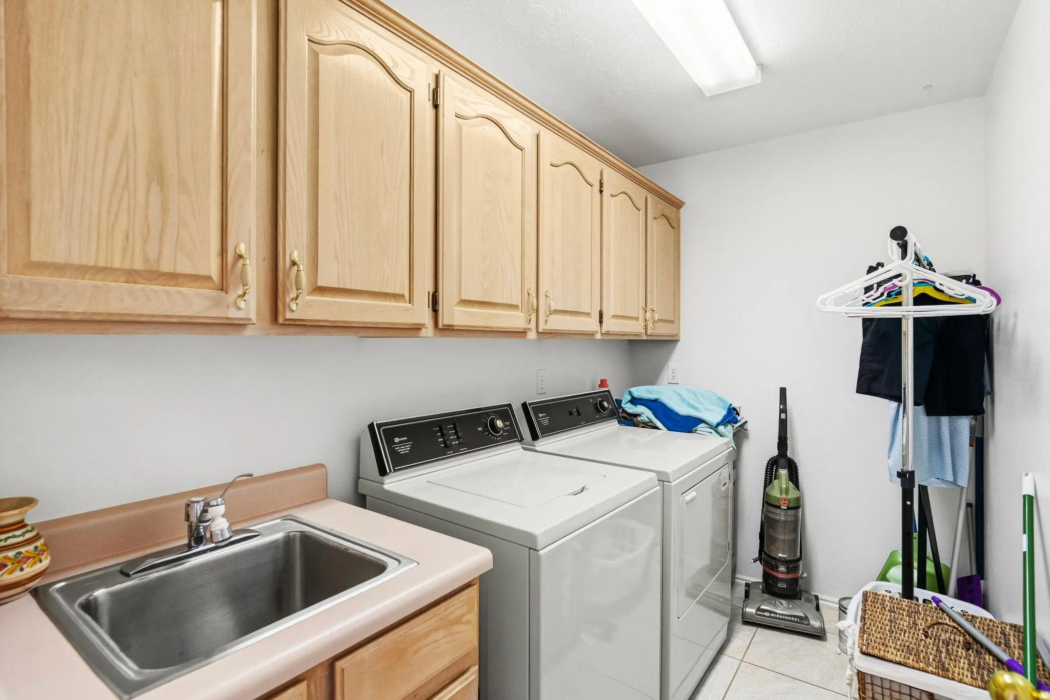 Laundry room featuring light wood cabinetry, a utility sink with a laminate countertop, and neutral tile flooring