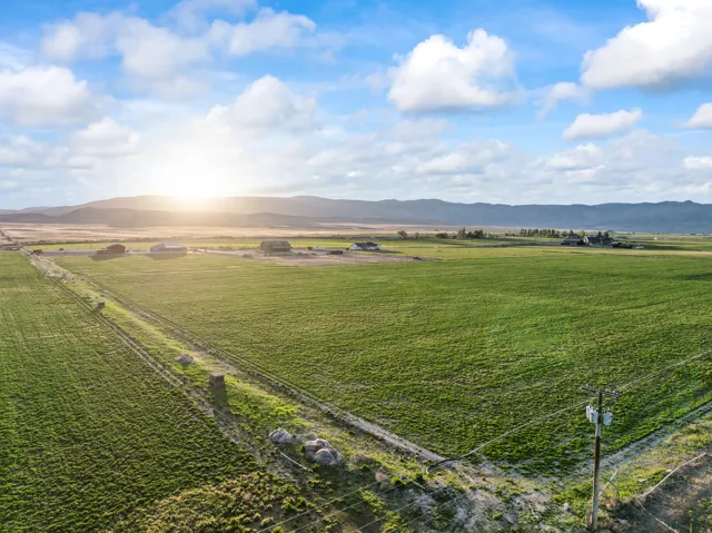 Expansive green fields extending towards distant mountains, with scattered agricultural structures