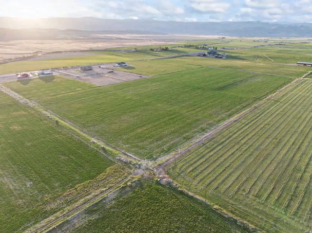 Expansive agricultural land featuring cultivated fields, distant homes, and mountain range backdrop