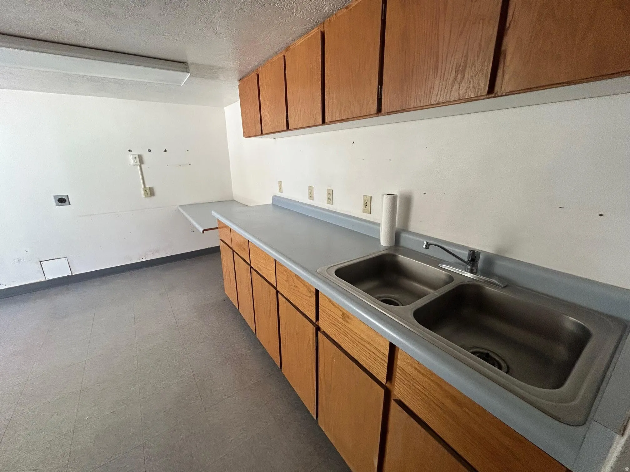 Utility space featuring a double basin stainless steel sink, wood cabinetry, and a light-toned countertop