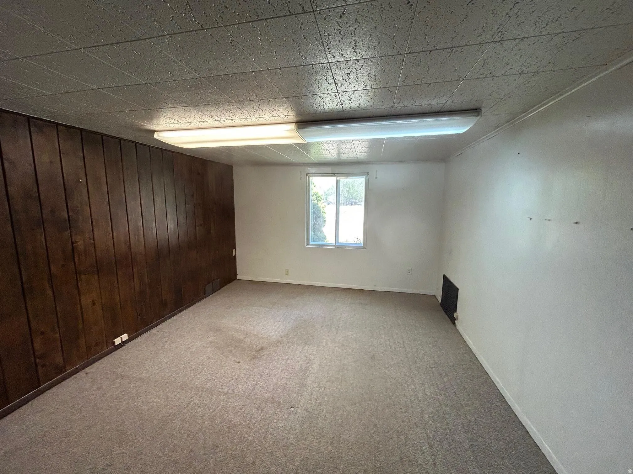 Room with wood-panel accent wall, neutral carpet flooring, and a drop ceiling