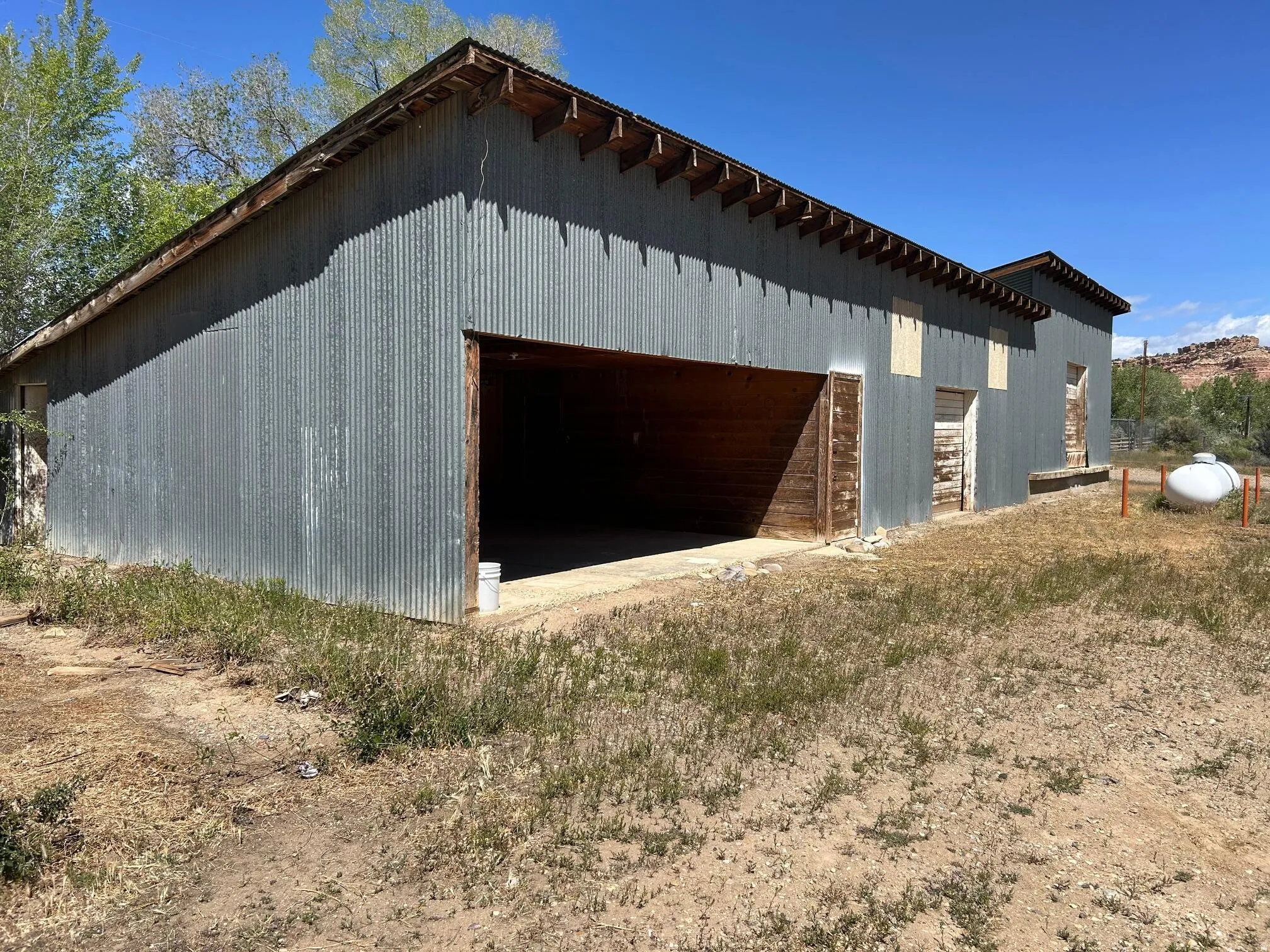 Corrugated metal-sided structure with exposed rafter tails, a large open bay entrance, and multiple additional entry points