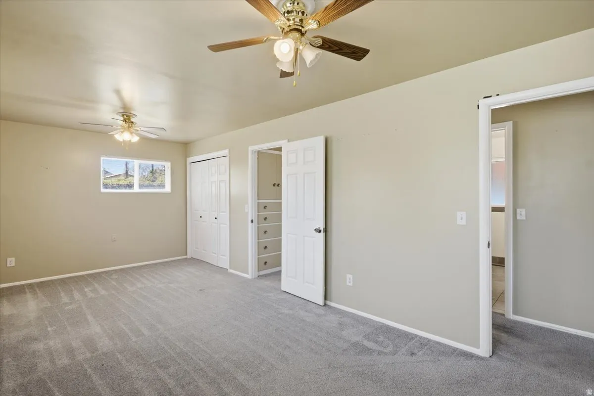 Spacious room featuring neutral wall tones, grey carpeting, two ceiling fans, and bi-fold closet doors