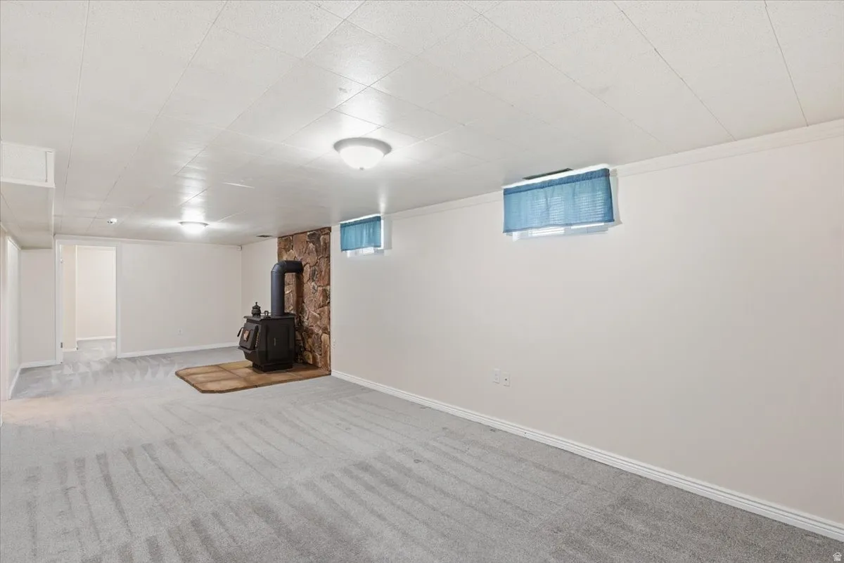 Spacious room featuring a central wood-burning stove with a stone surround, light gray patterned carpeting, and white painted walls