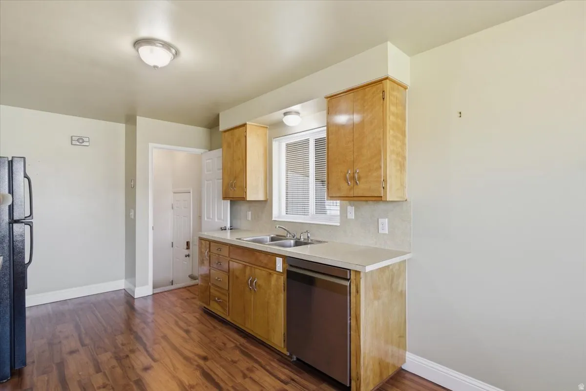 Kitchen featuring wood-finish flooring, light-toned cabinetry, a stainless steel dishwasher, a double basin sink, and a window with blinds
