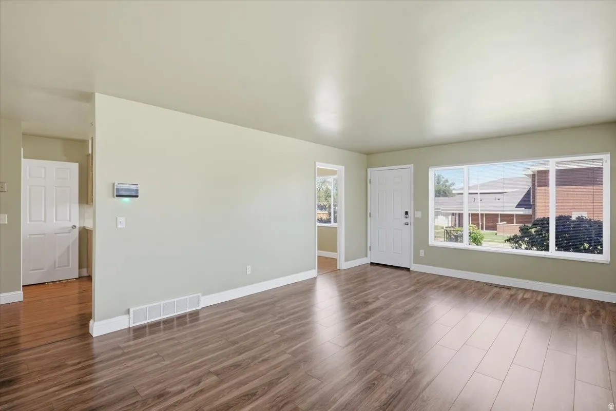 Spacious living area featuring wood-finish flooring, a large picture window, and a white paneled entry door