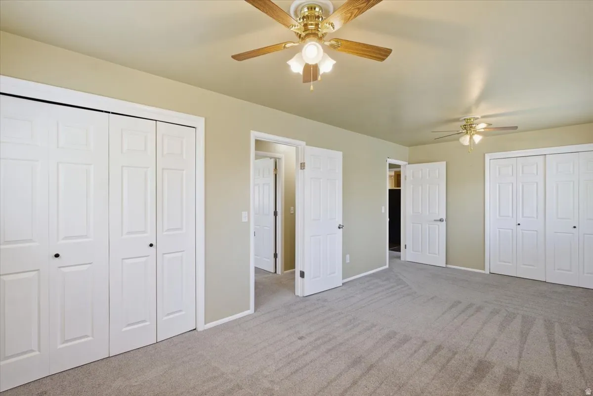Carpeted room featuring multiple ceiling fans with light kits, two sets of bi-fold closet doors, and two interior doors