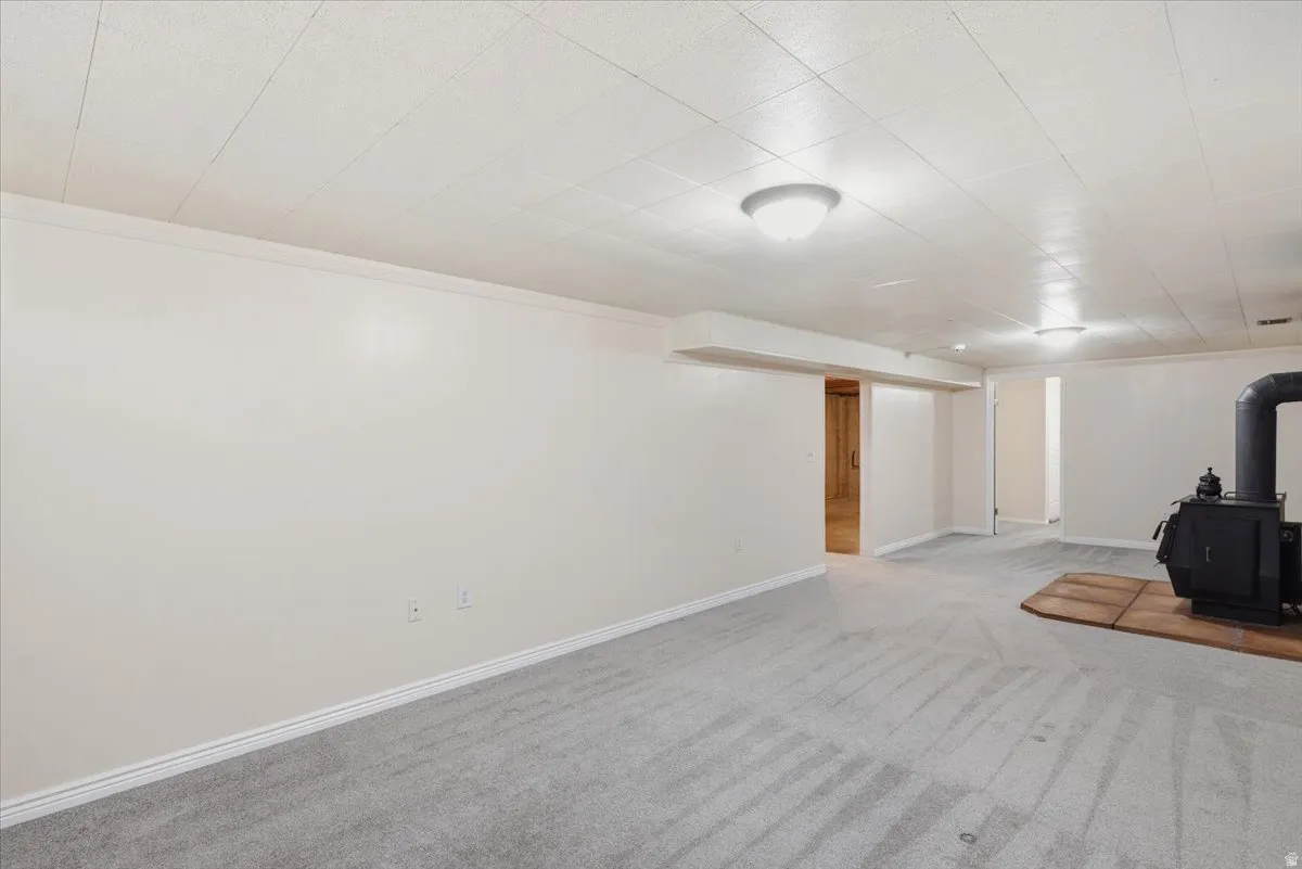 Spacious lower-level room featuring light gray carpeting, white walls, and a drop ceiling