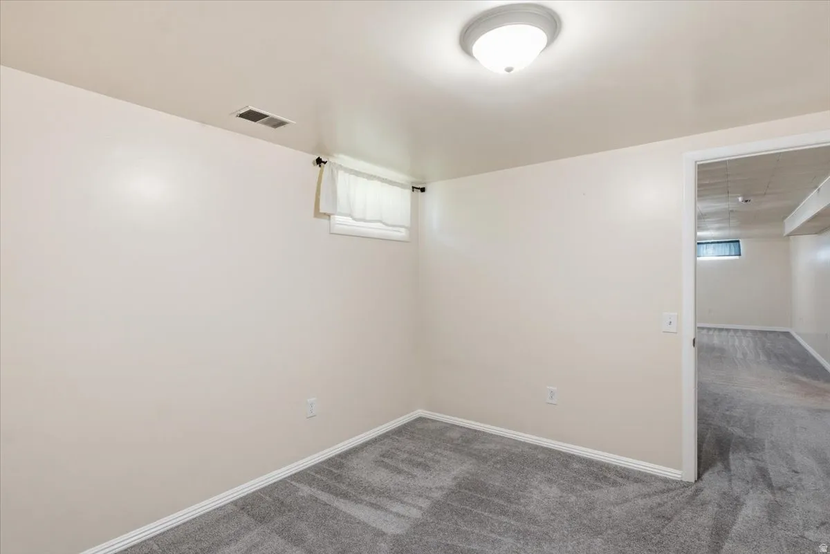 Room featuring new gray carpet, neutral painted walls, a flush-mount ceiling light, white baseboards, and a window with white Roman shades
