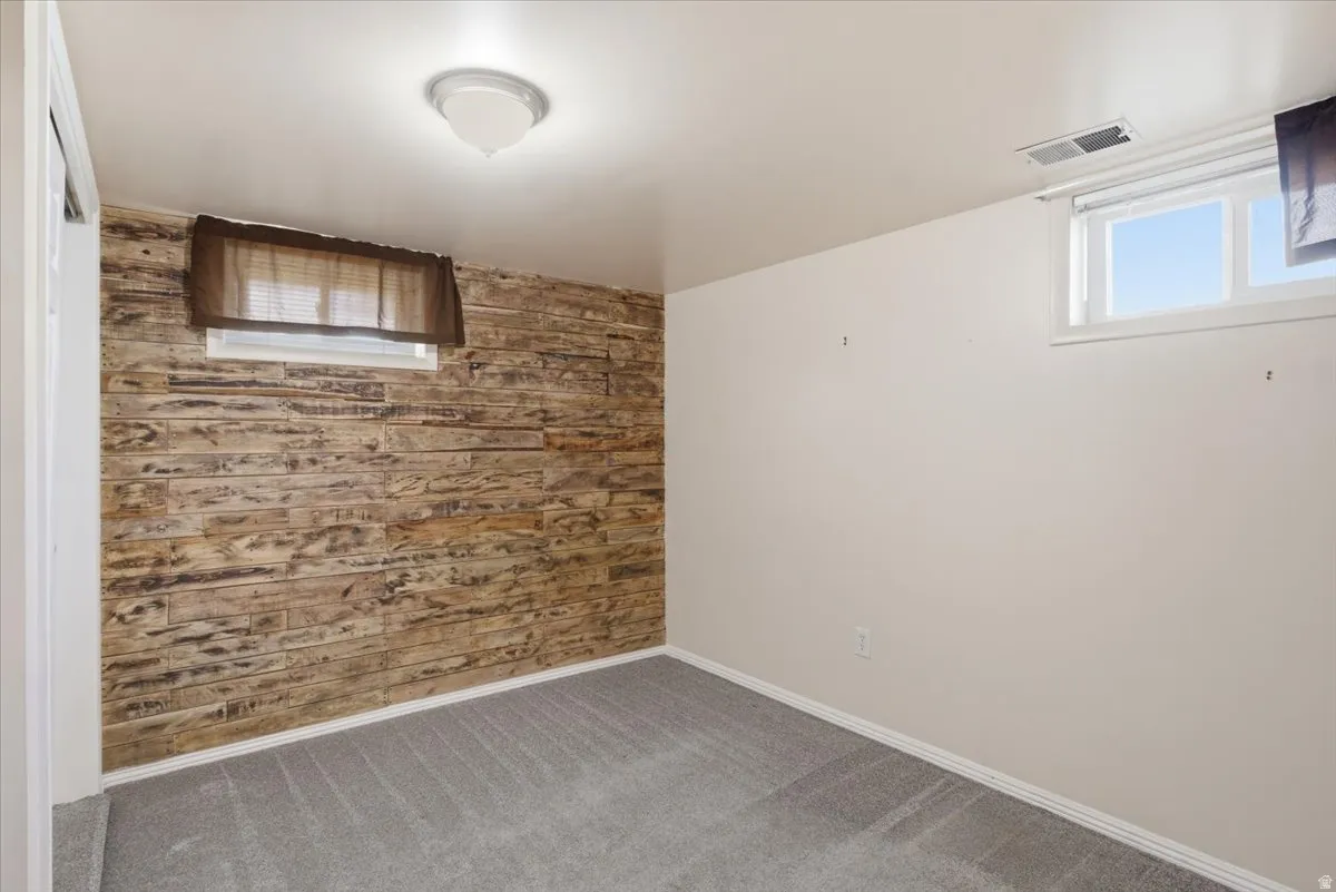 Accent wall featuring natural wood-look paneling, gray carpet flooring, white baseboards, and a flush-mount ceiling light
