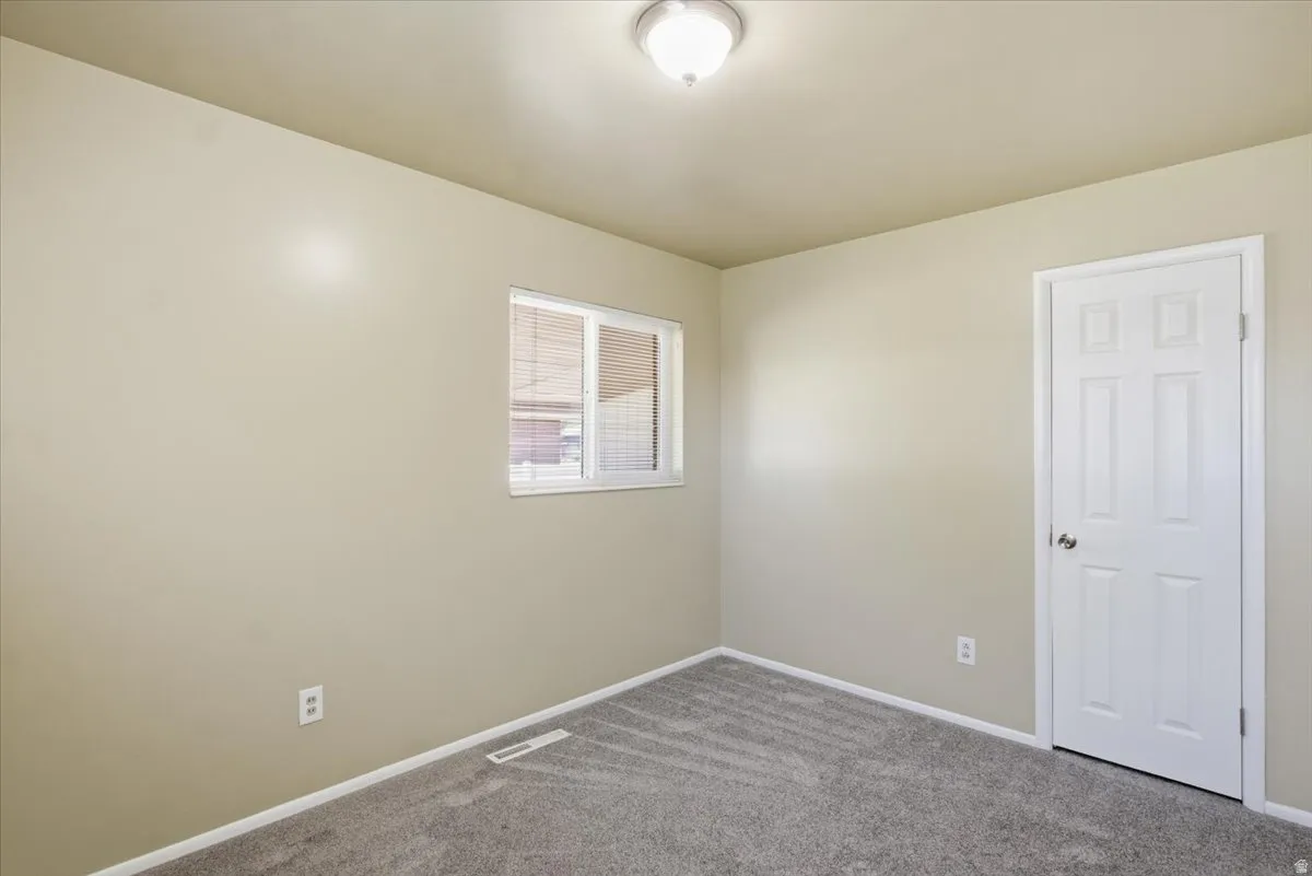 Interior room featuring neutral wall paint, gray patterned carpeting, white baseboards, and a white six-panel door with a round silver-toned knob