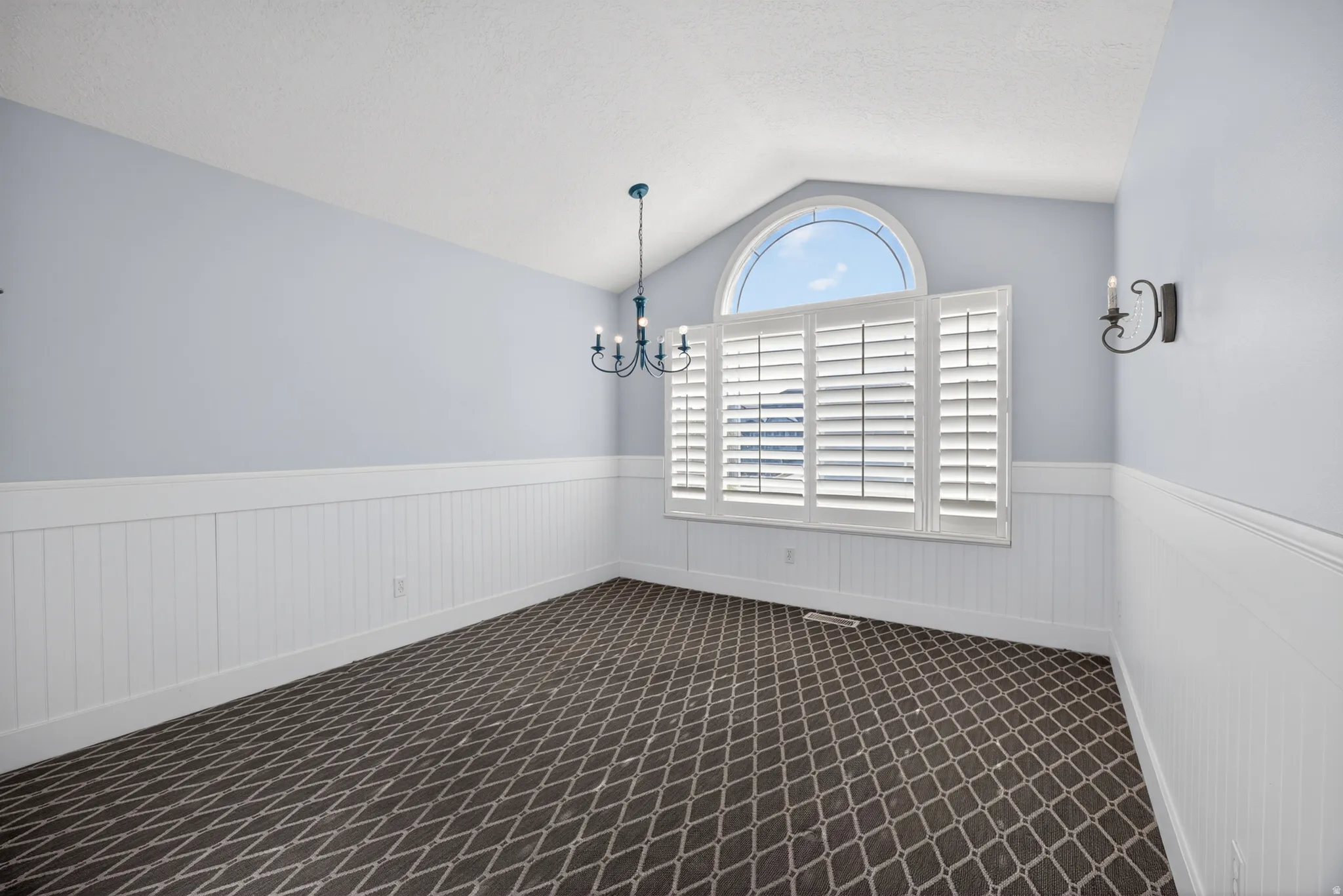 Arched window with plantation shutters, vaulted ceiling, and decorative chandelier