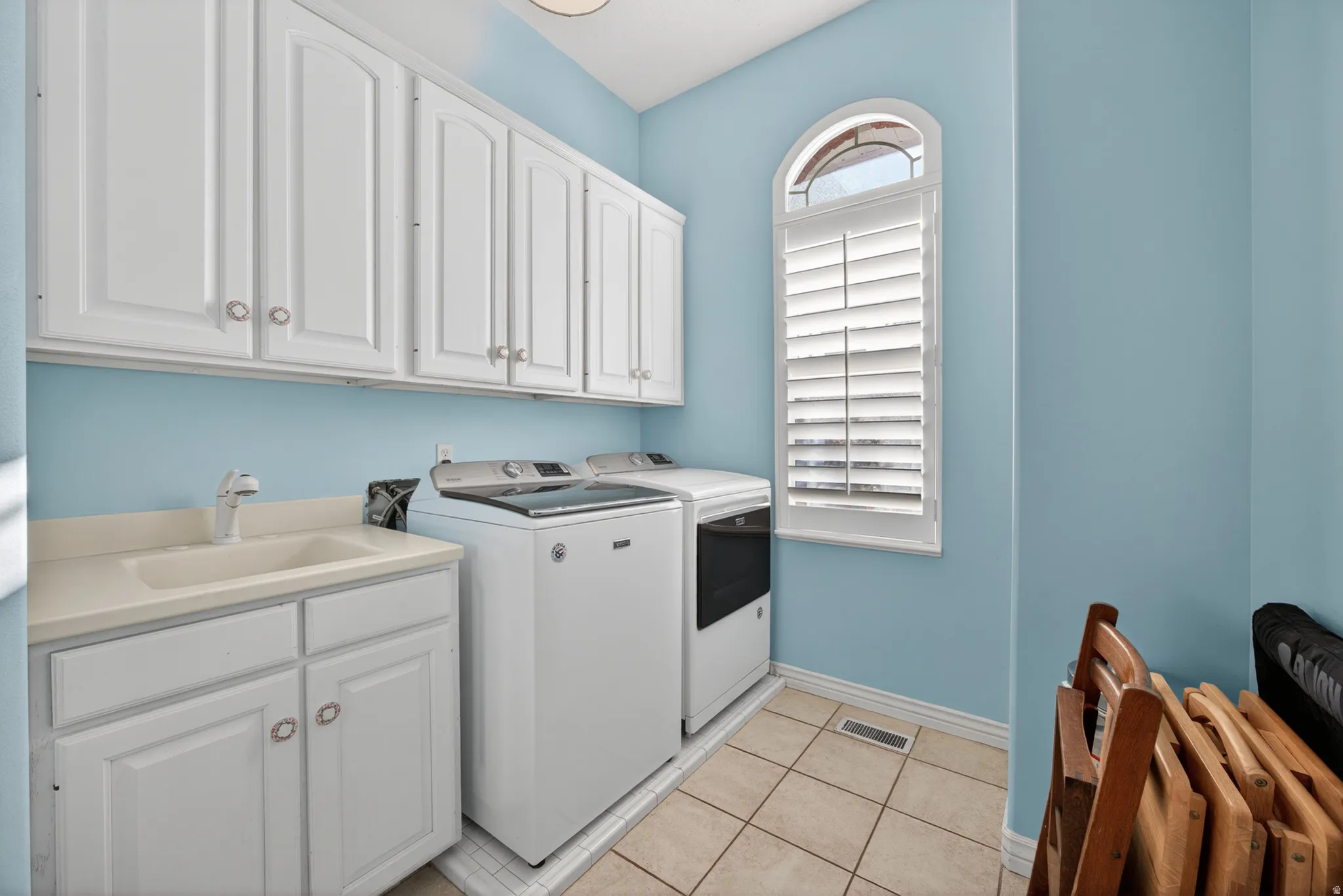 Laundry room with white upper and lower cabinetry, utility sink, and tiled flooring