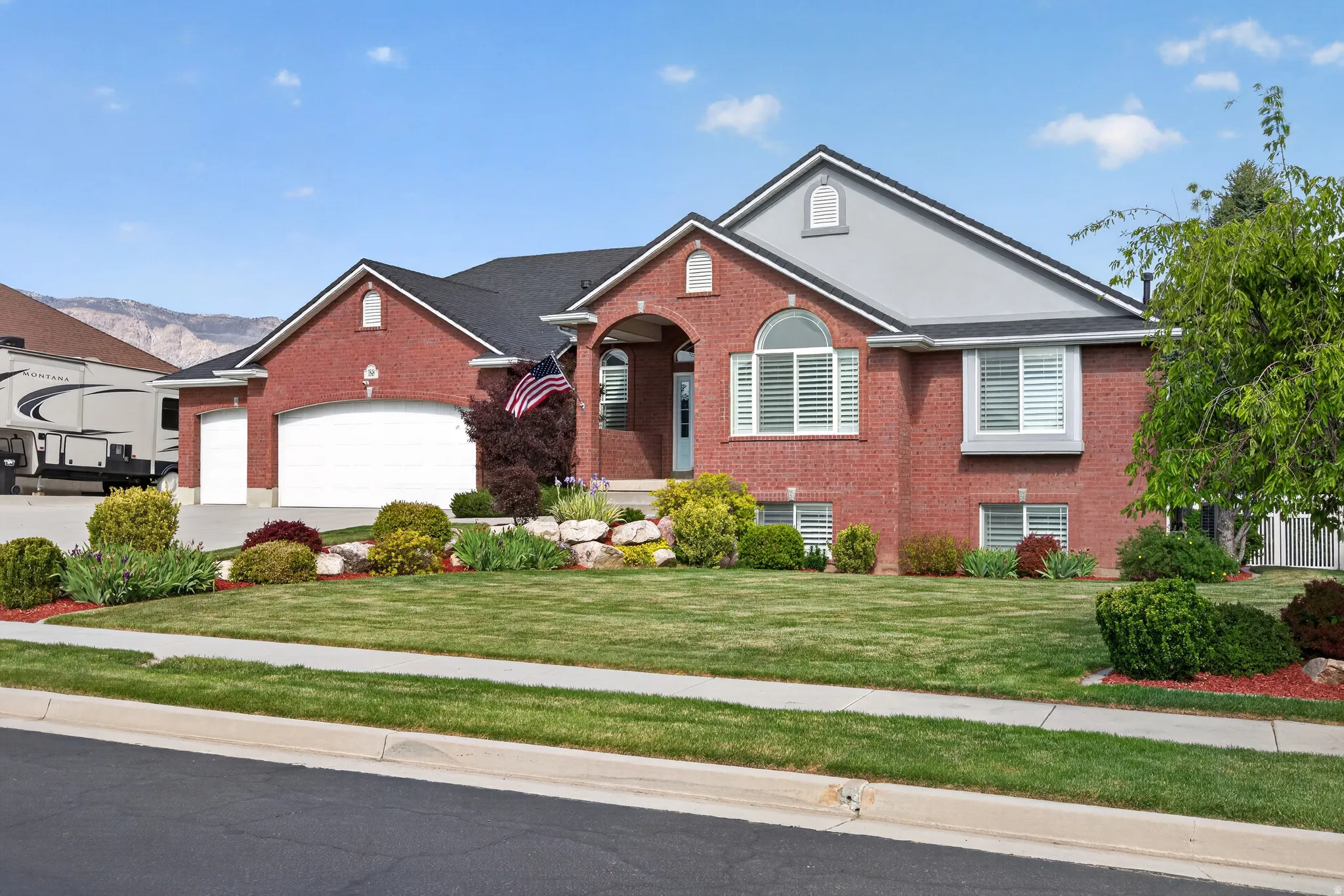 Brick exterior with an arched entry, multiple garage bays, and a well-manicured lawn with mature landscaping