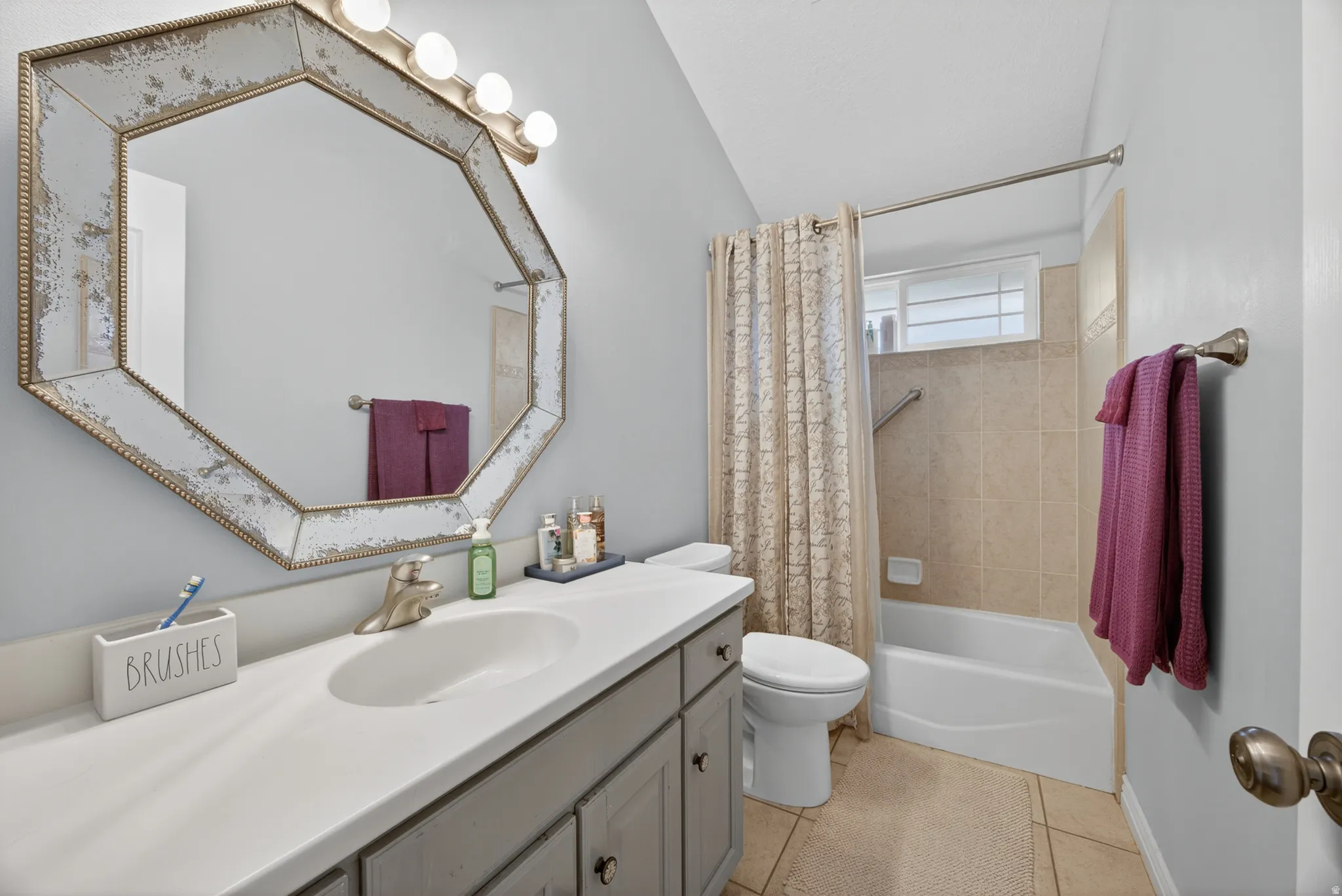 Bathroom featuring a full vanity with an integrated sink, a large octagonal mirror, and a tub-shower combination with tile surround