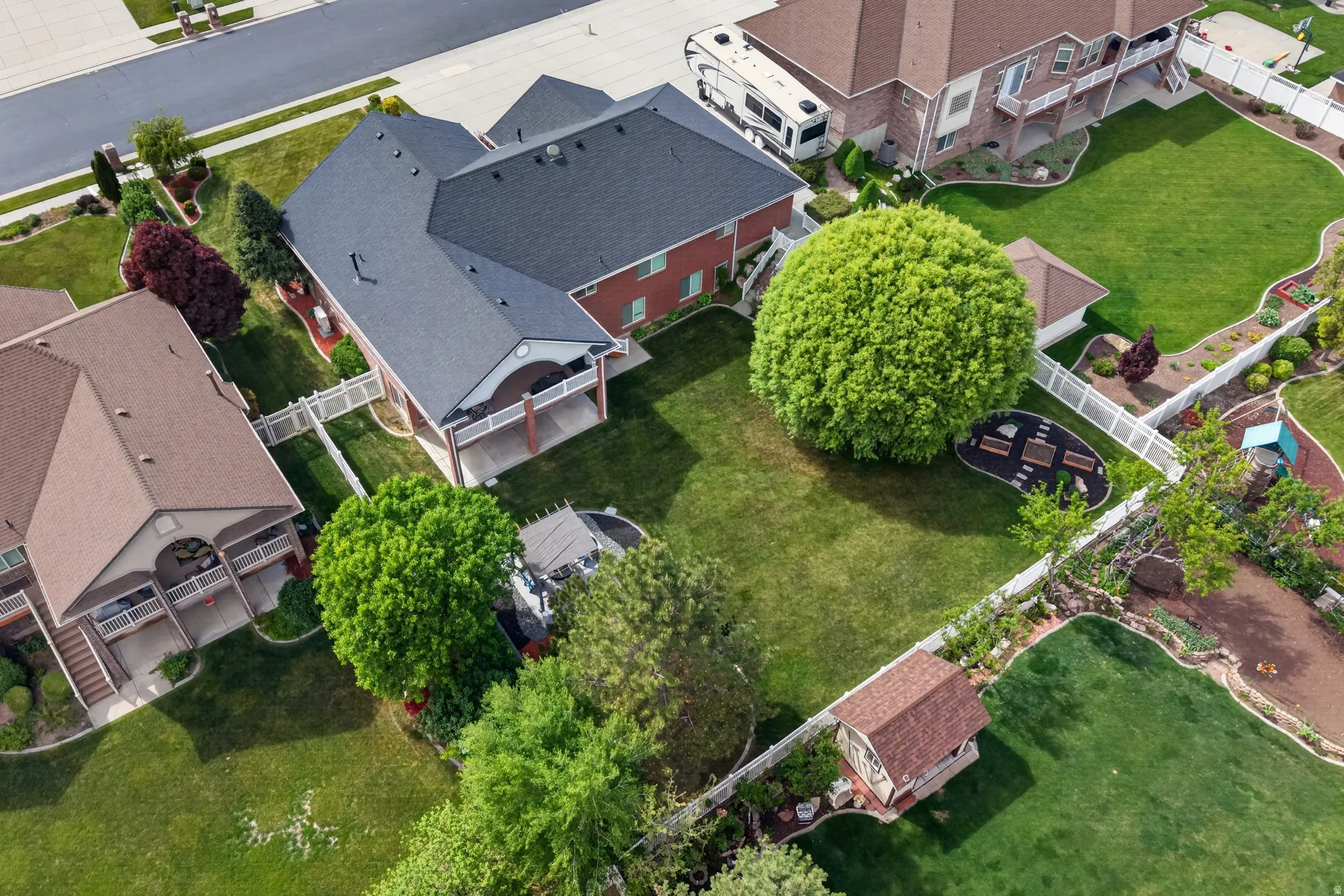 Expansive backyard featuring a manicured lawn, mature trees, a dedicated fire pit area with seating, and a white vinyl fence perimeter