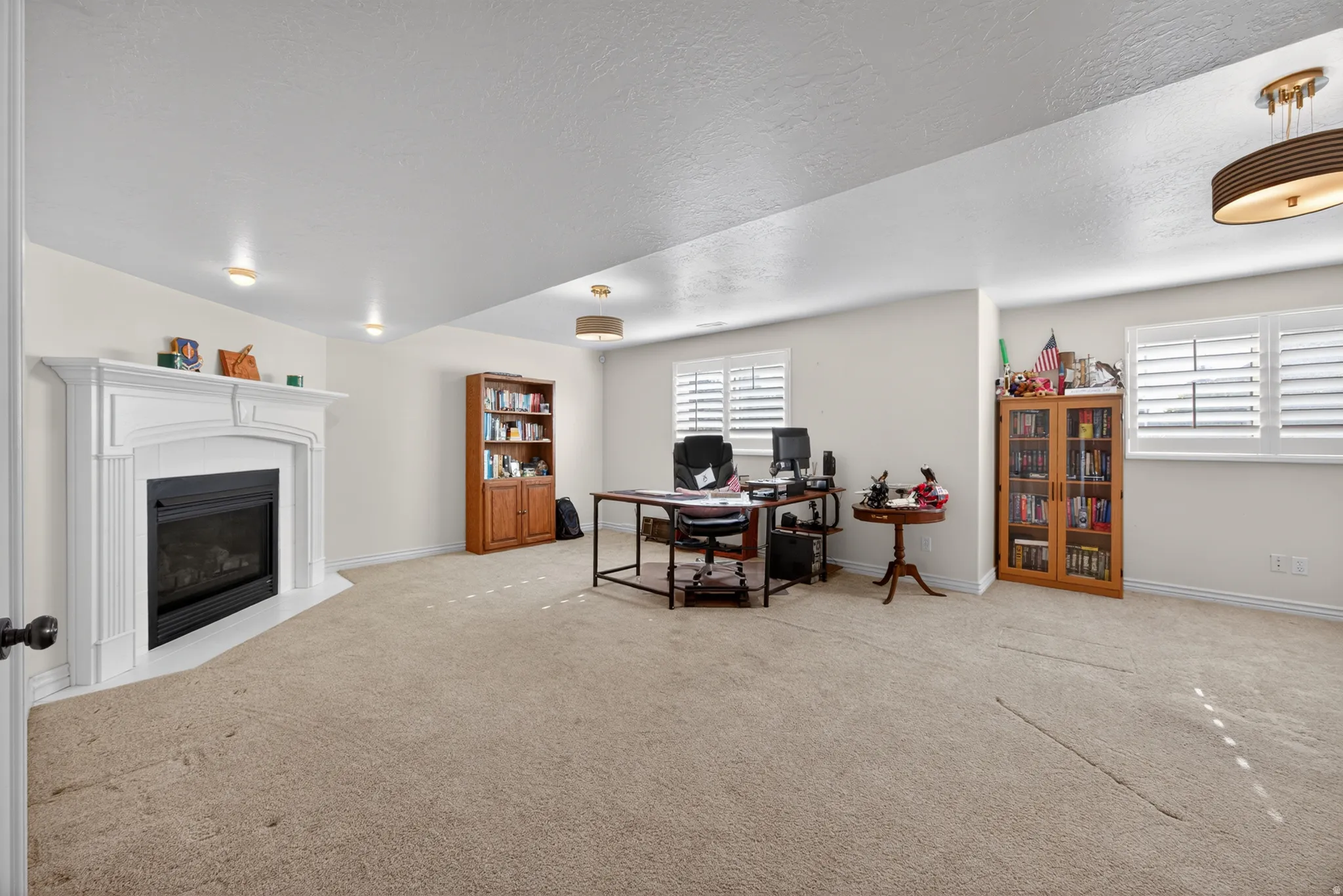 Spacious interior featuring a gas fireplace with a white mantel, light-toned carpeting, recessed lighting, and windows equipped with white plantation shutters