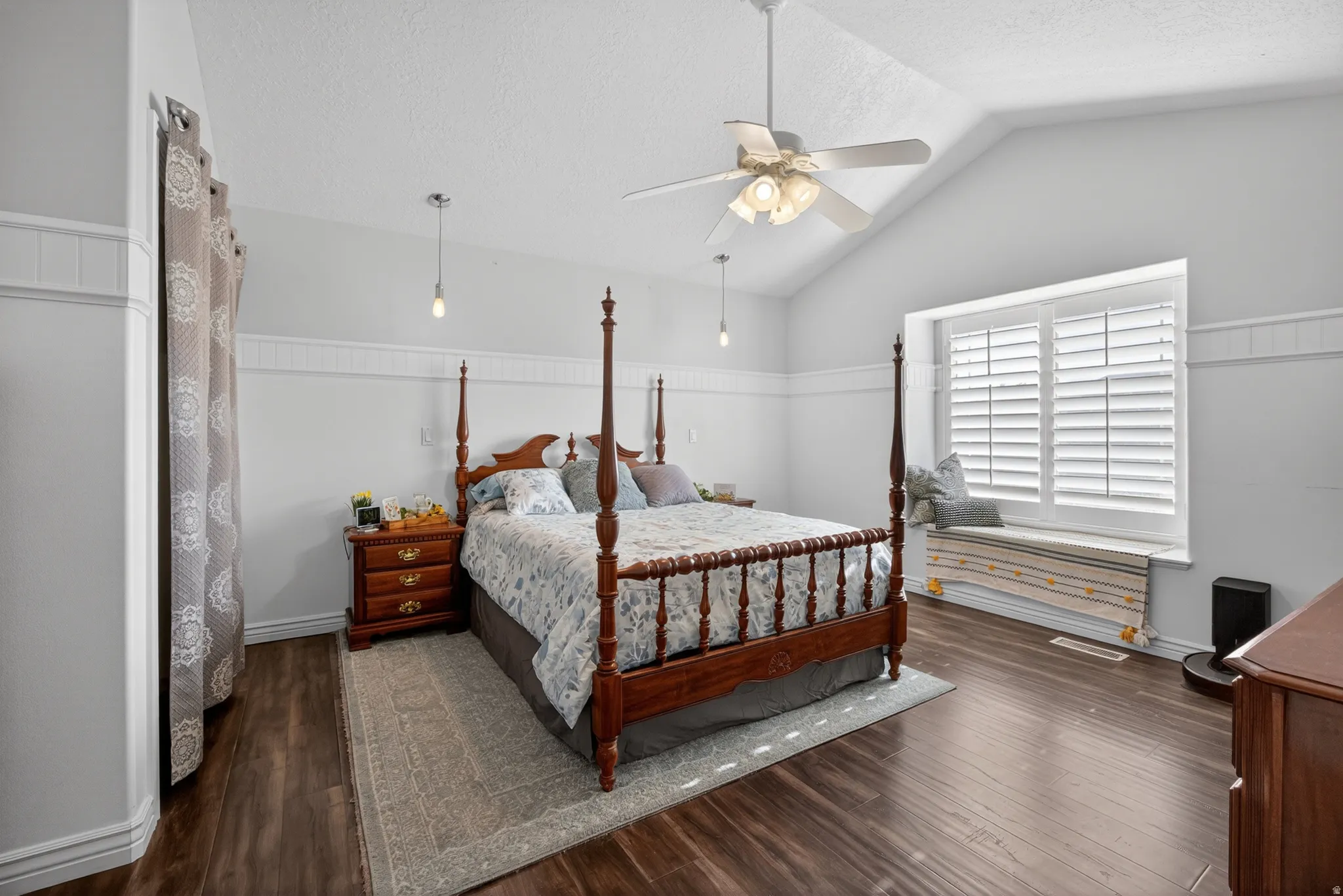 Vaulted ceiling bedroom featuring wood-finish flooring and a window seat with plantation shutters