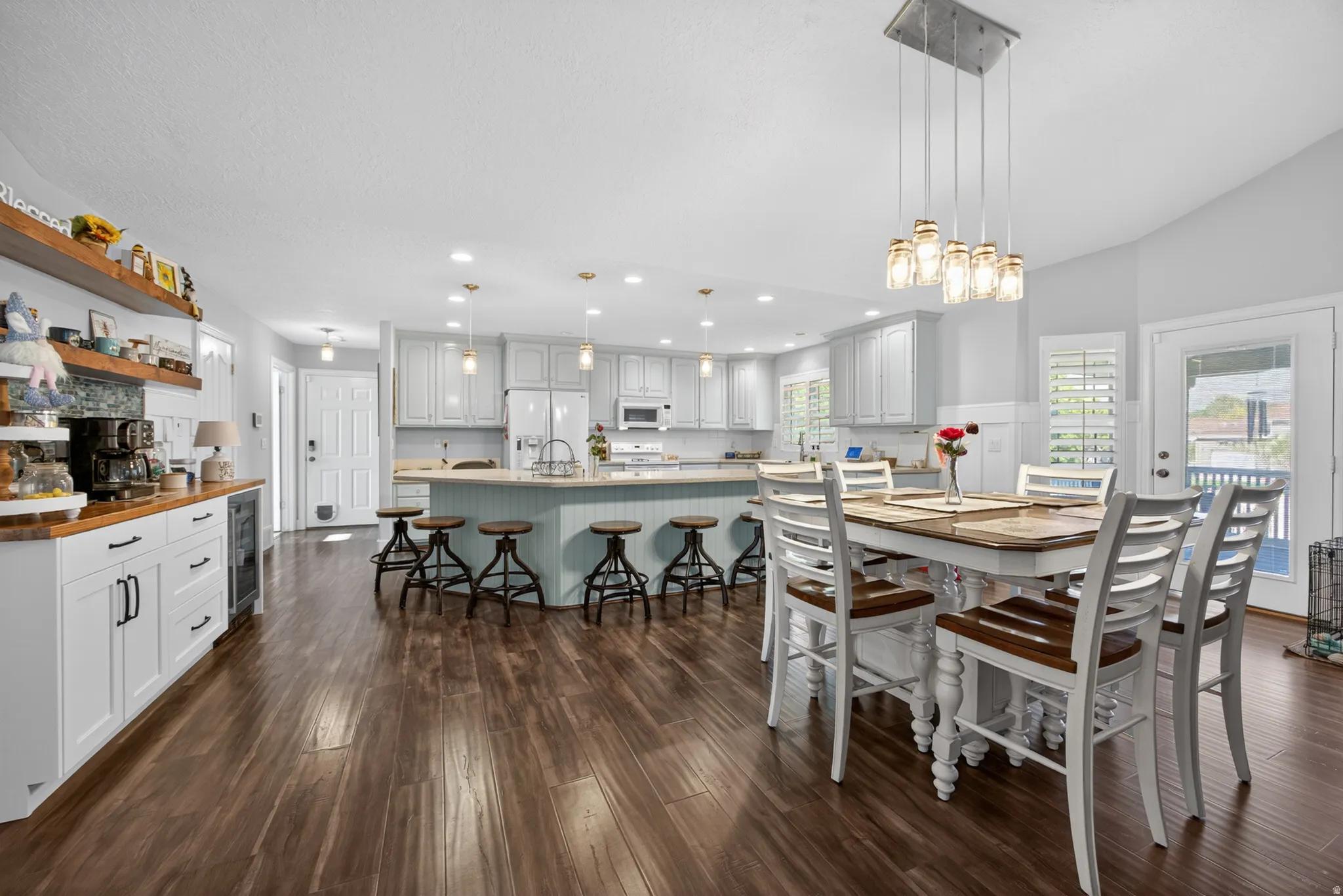 Open-concept kitchen and dining area featuring wood-finish flooring, a spacious kitchen island with seating, light cabinetry, and an integrated beverage cooler