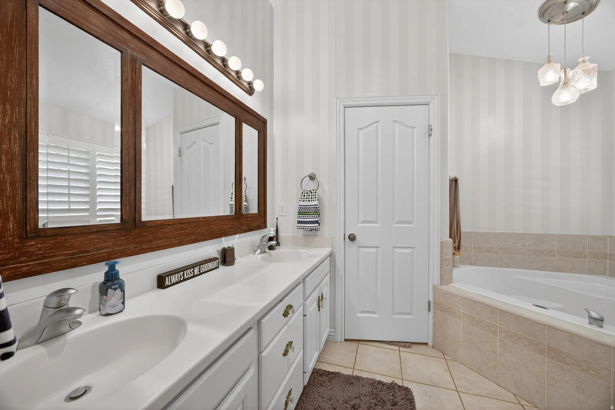 Bathroom featuring a double vanity with white cabinetry, a large framed mirror, and a built-in tub with tile surround