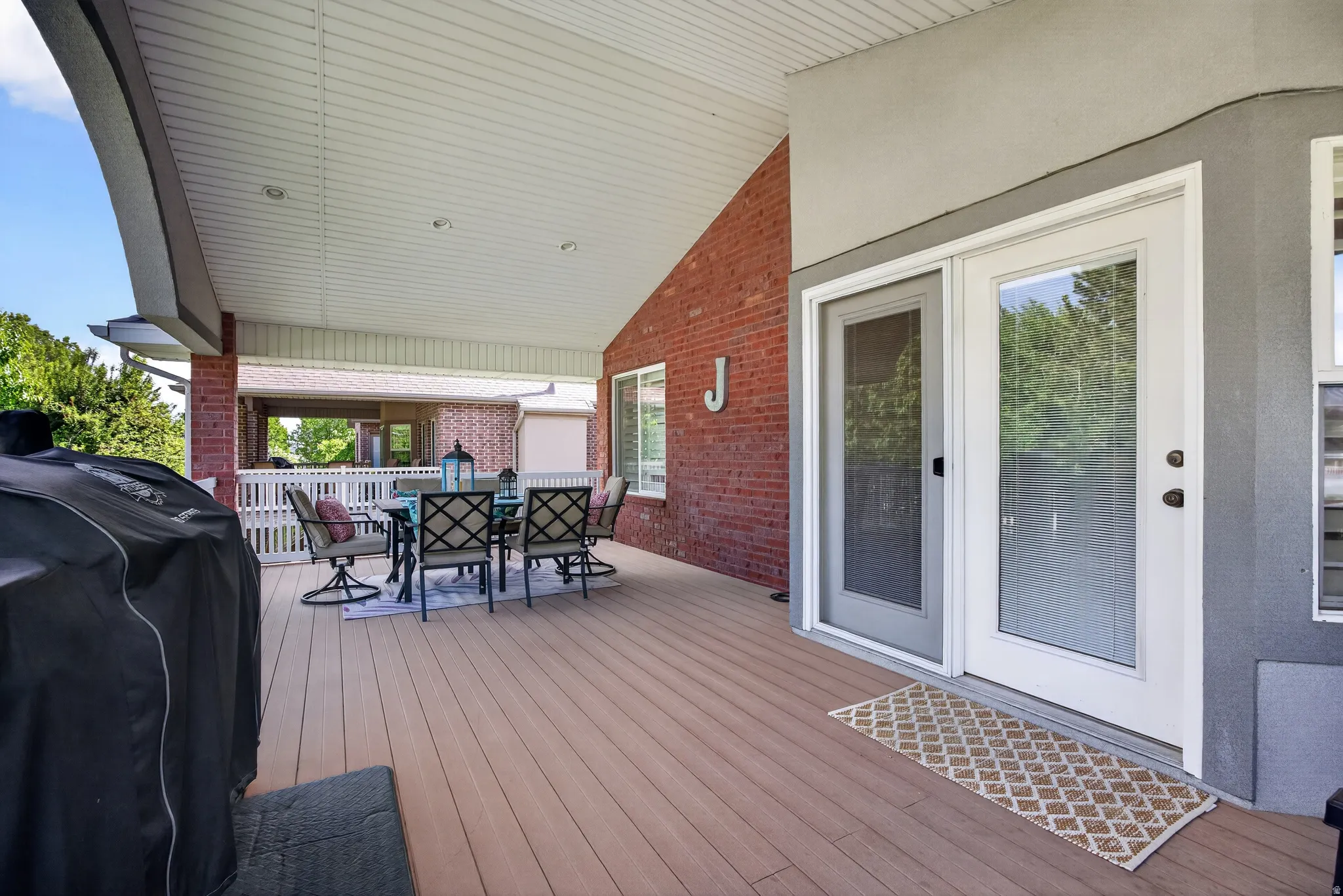 Spacious covered deck featuring composite decking, brick exterior wall, recessed lighting, and white French doors with screen