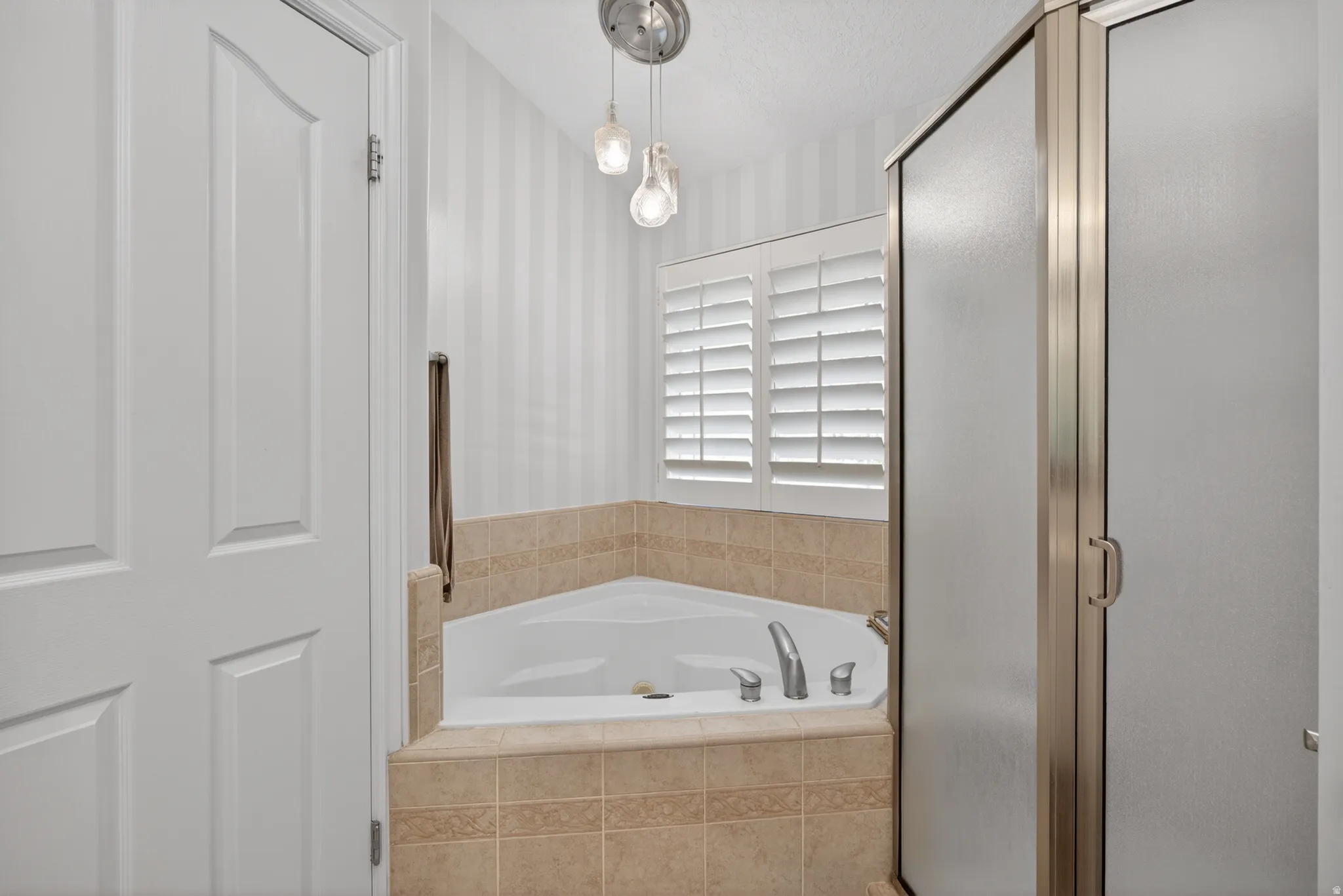 Corner soaking tub with tile surround, plantation shutters, and a frameless glass shower enclosure