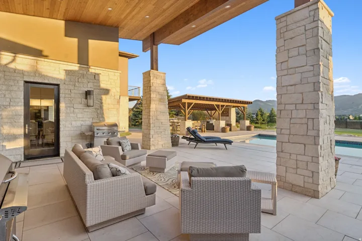 Expansive stone patio featuring a built-in outdoor kitchen area, a swimming pool, and a dedicated pergola structure