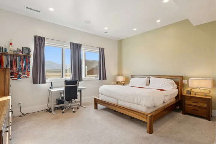 Bedroom featuring a large window, recessed ceiling lighting, light-colored carpeting, a wall-mounted speaker, and a wall-mounted vent