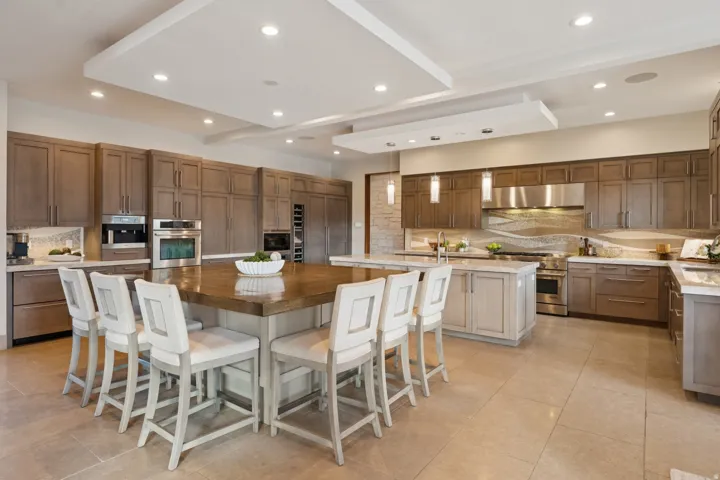 Expansive kitchen featuring a large central island with seating, extensive cabinetry, stainless steel appliances, and tray ceilings with recessed lighting