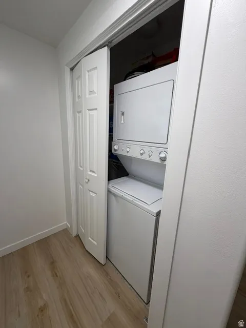 Laundry closet with bi-fold doors, white stacked washer and dryer, and wood-finish flooring
