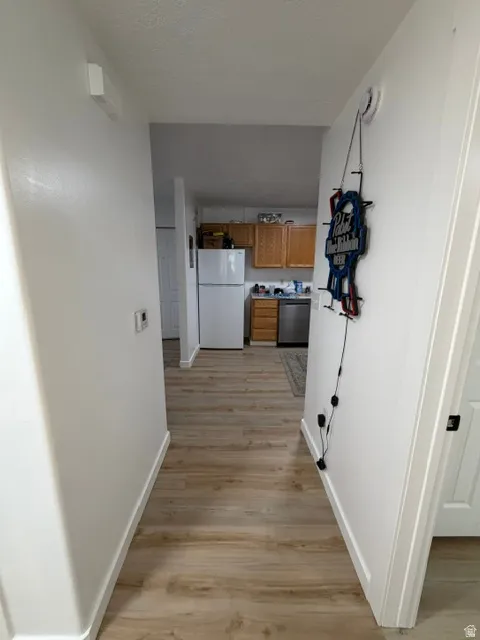 Hallway featuring wood-finish flooring, white baseboards, and a neutral wall color, opening to a kitchen with wood cabinetry and stainless steel appliances