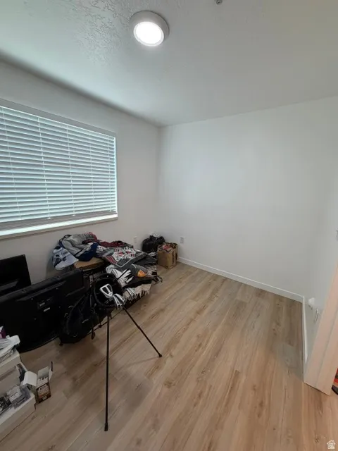 Room featuring light wood-finish flooring, white walls, and a window with blinds
