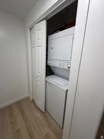 Laundry closet with bi-fold doors, white stacked washer and dryer, and wood-finish flooring