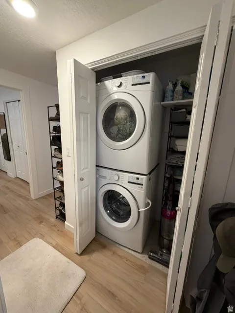 Dedicated laundry closet featuring a stackable washer and dryer, built-in shelving, and wood-finish flooring
