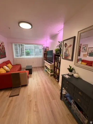 Spacious living area featuring wood-finish flooring, a large window with vertical blinds, and a flush-mount ceiling light