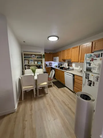 Kitchen and dining area featuring wood-finish flooring, white appliances, and oak cabinetry