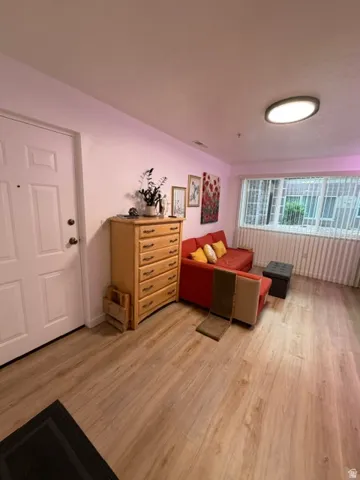 Open-concept living space featuring wood-finish flooring, a contemporary flush-mount ceiling light, and a bright window with horizontal blinds
