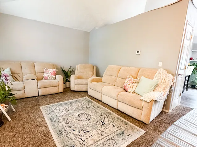 Spacious living area featuring a vaulted ceiling, neutral wall tones, and mixed flooring with wood-finish planks and carpeting