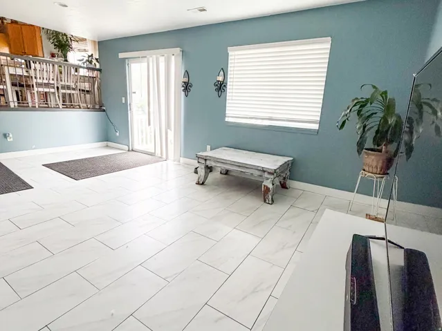 Spacious living area featuring light-toned  tile flooring, blue accent wall, recessed ceiling lighting, and sliding glass door
