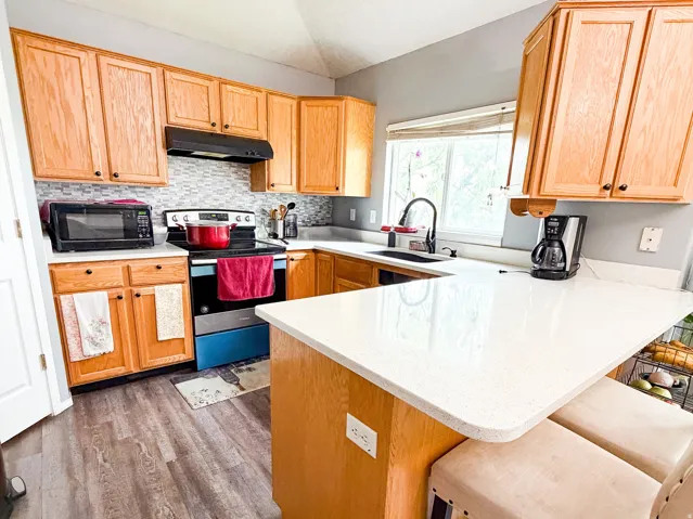 Kitchen featuring wood-finish flooring, light wood cabinetry, white countertops, and a gray tile backsplash