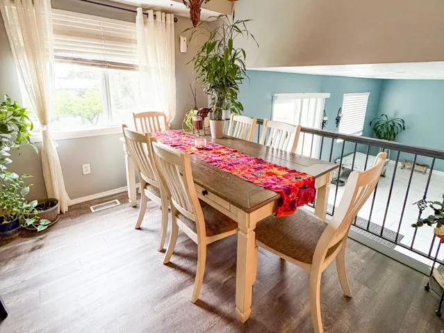 Dining area featuring wood-finish flooring, a decorative chandelier, and a large window with blinds and sheer curtains