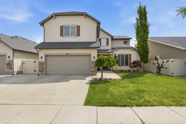 Stucco exterior with stone accents, featuring a two-car garage, mature front yard landscaping, and a concrete driveway