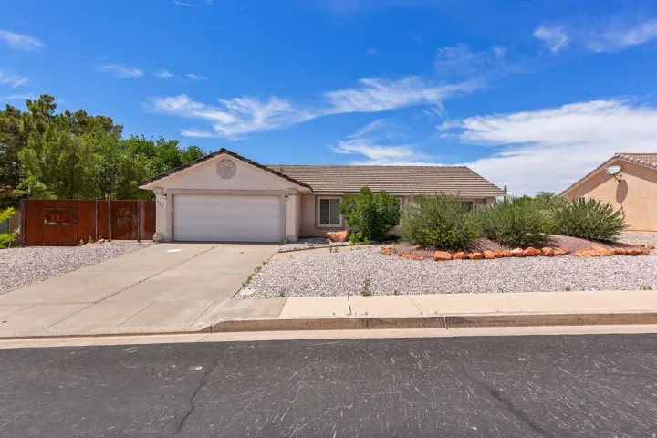 Single-story residence featuring a concrete driveway, an attached garage with a white door, and a low-maintenance gravel and rock front yard with established shrubbery