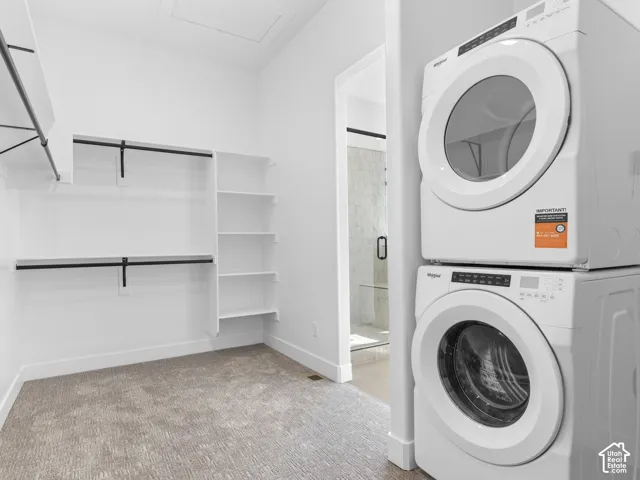 Built-in shelving, hanging rods, carpet flooring, and a stacked washer and dryer