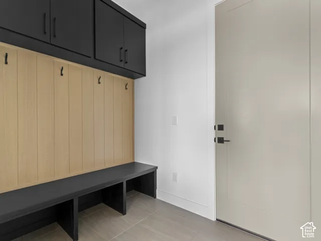 Built-in mudroom bench with three storage cubbies, matte black upper cabinetry, light wood-finish wainscoting, and tile flooring