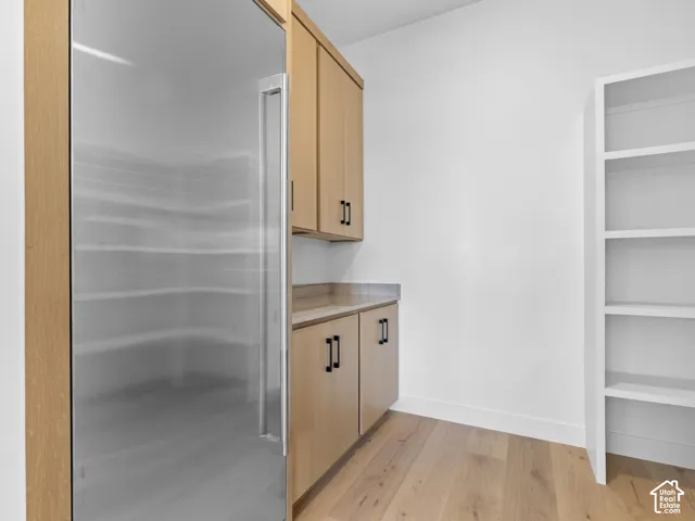 Built-in stainless steel refrigerator, light wood-finish cabinetry, solid surface countertop, white built-in shelving, and wood-finish flooring