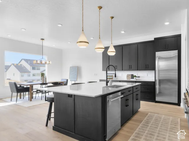 Spacious kitchen featuring dark cabinetry, stainless steel appliances, a center island with a sink, and pendant lighting