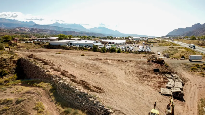 Expansive cleared land parcel featuring a retaining wall, visible highway access, and distant mountain scenery