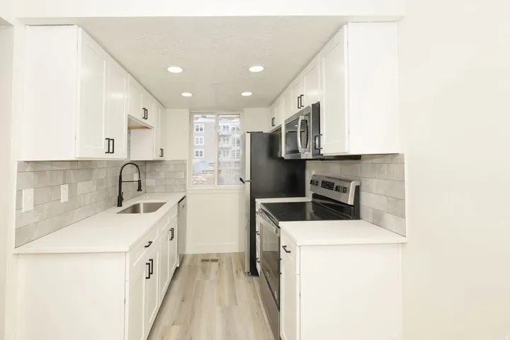 Galley kitchen featuring white cabinetry, light-toned countertops, and a subway tile backsplash